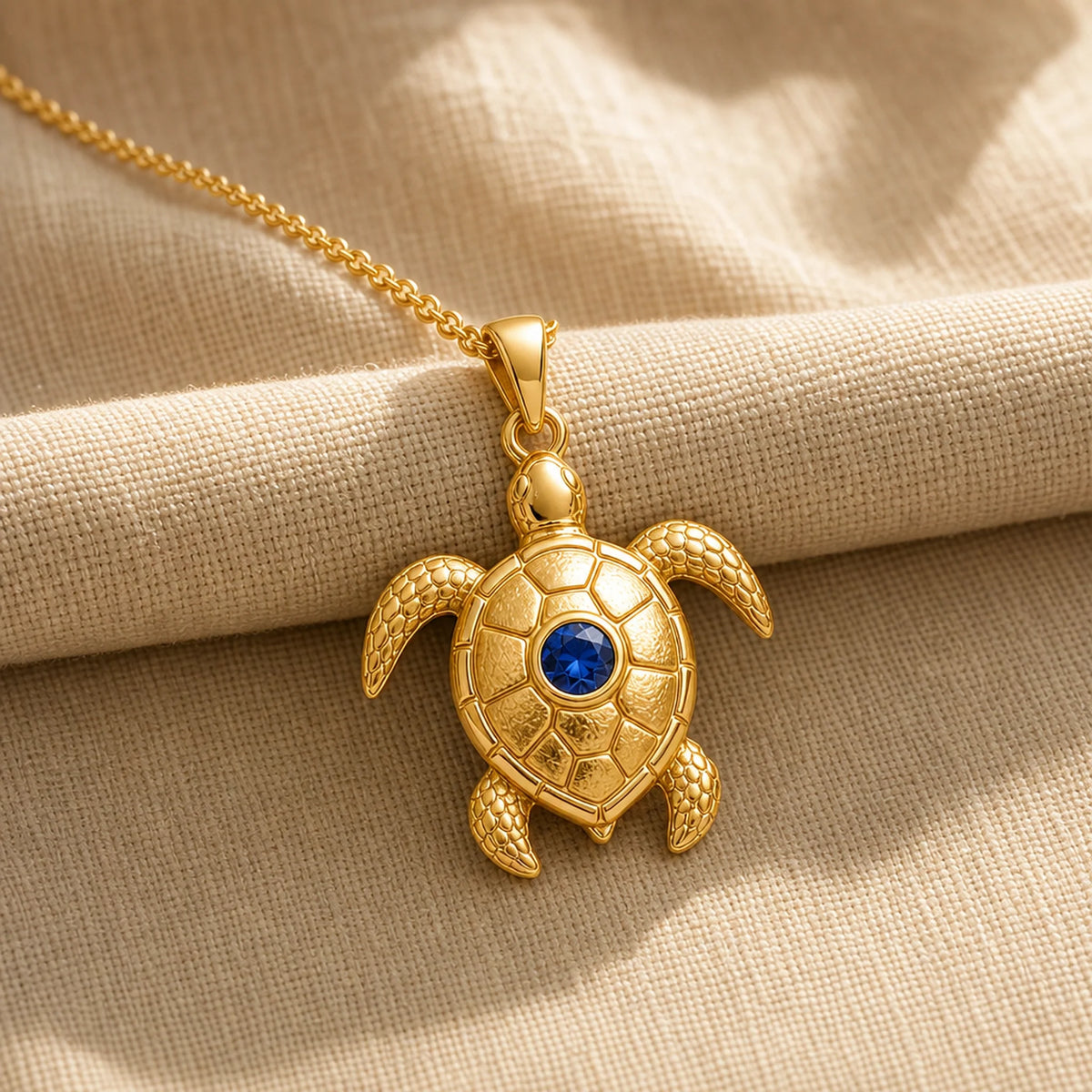 925 sterling silver sea turtle pendant with patterned shell plates, textured flippers and a round blue sapphire centerpiece. Gold finish.
