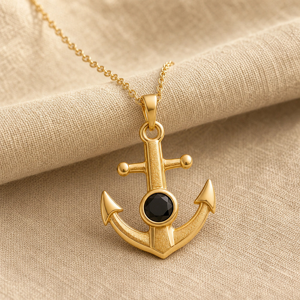Black onyx anchor pendant with a faceted dark stone in a round bezel setting, raised textured center, polished arrowhead flukes, and cable chain. Gold finish.