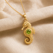 925 sterling silver seahorse pendant with a curled tail, sculpted marine details and a round green peridot centerpiece. Gold finish.