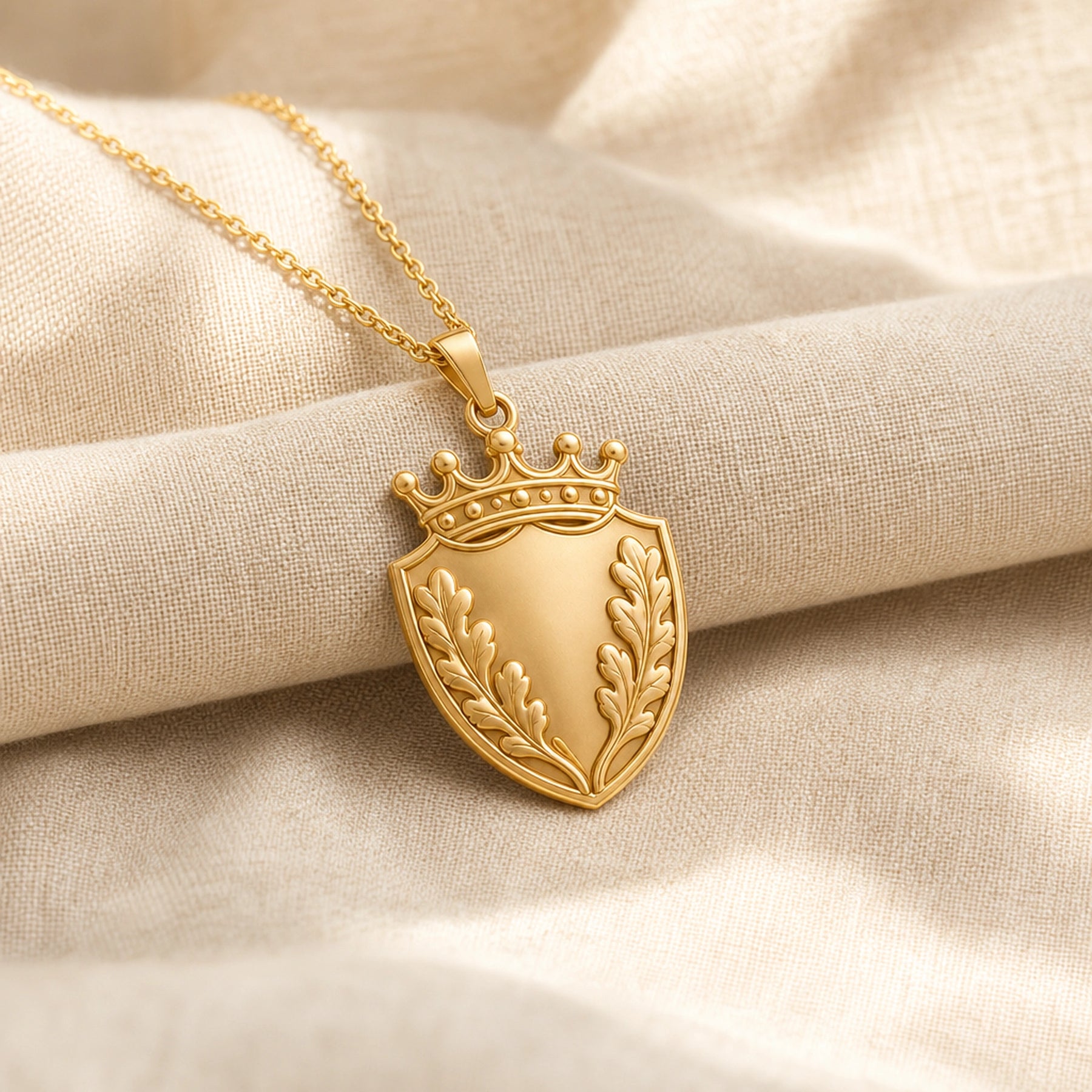 Oakleaf crown shield pendant with a pointed shield shape, raised botanical leaf relief, detailed crown top, smooth center panel, and a polished cable chain. Gold finish.