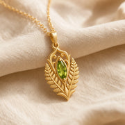 Marquise peridot fern pendant with a vivid green faceted stone in a smooth setting, framed by raised elven fern leaves, openwork scrolls, and botanical relief details. Gold finish.