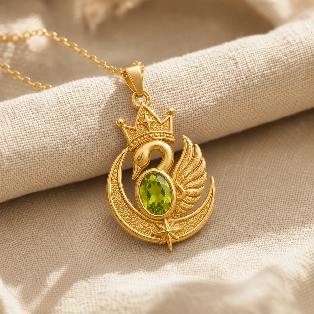 Peridot moon swan crown pendant with an oval green stone in a framed setting, detailed crowned swan, textured crescent moon, raised wing, and star accents. Gold finish.