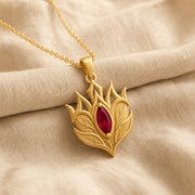 Ruby Elven Crownleaf pendant with layered engraved leaf details, pointed crown-like shapes, and a deep red marquise-shaped stone in a raised central setting. Gold finish.
