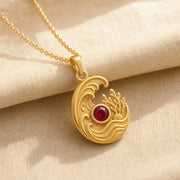 925 sterling silver tide pendant with curling ocean waves, coral and shell details, and a round ruby centerpiece. Gold finish.