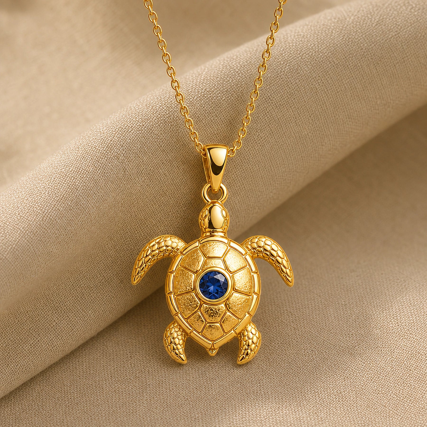 925 sterling silver sea turtle pendant with patterned shell plates, textured flippers and a round blue sapphire centerpiece. Gold finish.