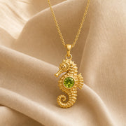925 sterling silver seahorse pendant with a curled tail, sculpted marine details and a round green peridot centerpiece. Gold finish.