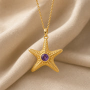 925 sterling silver five-arm starfish pendant with raised bead texture and a round purple amethyst centerpiece. Gold finish.