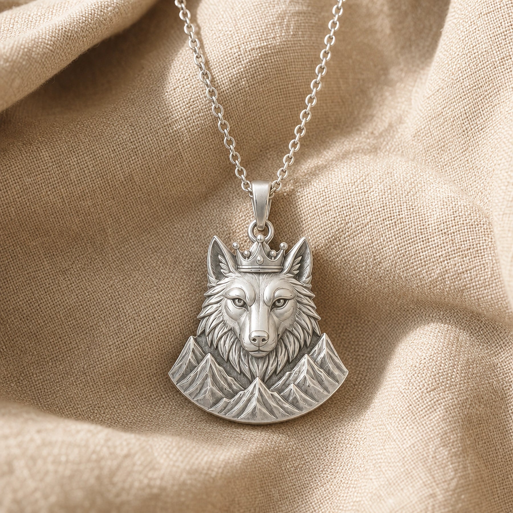 Crowned alpine wolf pendant in a warm yellow finish, showing a detailed wolf head, raised crown, and sculpted mountain relief beneath the bail. Silver finish.