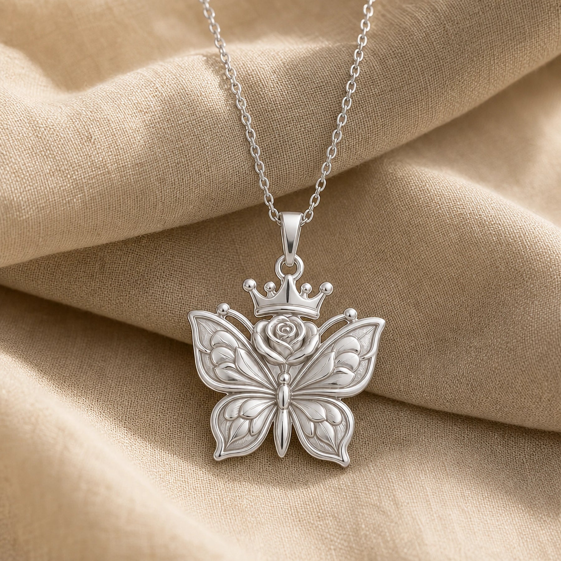 Rose-crowned butterfly pendant necklace with openwork textured wings, a raised floral rose, and a small crown above the butterfly in a warm polished finish. Silver finish.