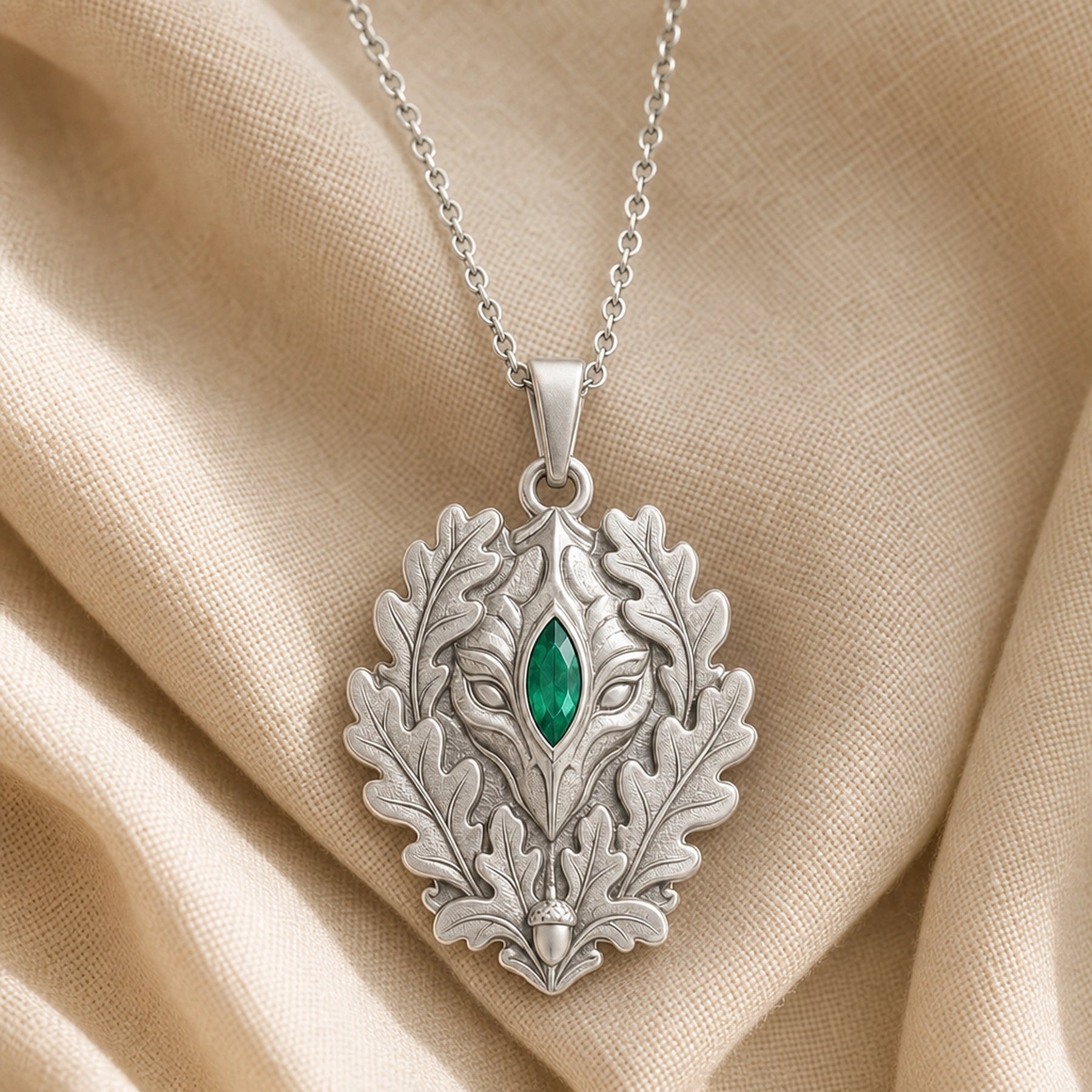 Marquise emerald oakleaf pendant with a vivid green stone set at the center of a sculpted guardian face, framed by raised oak leaves and an acorn detail. Silver finish.