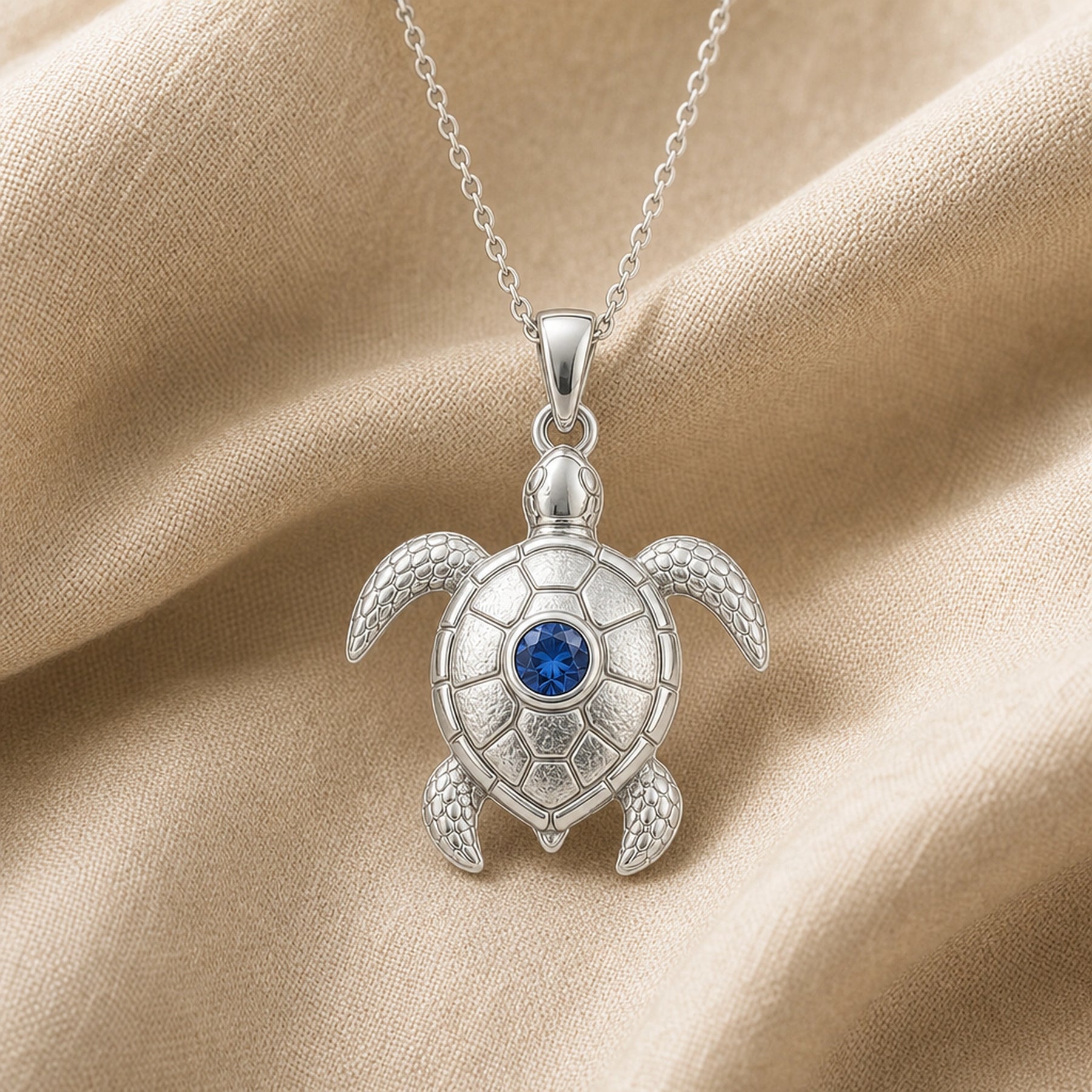 925 sterling silver sea turtle pendant with patterned shell plates, textured flippers and a round blue sapphire centerpiece. Silver finish.