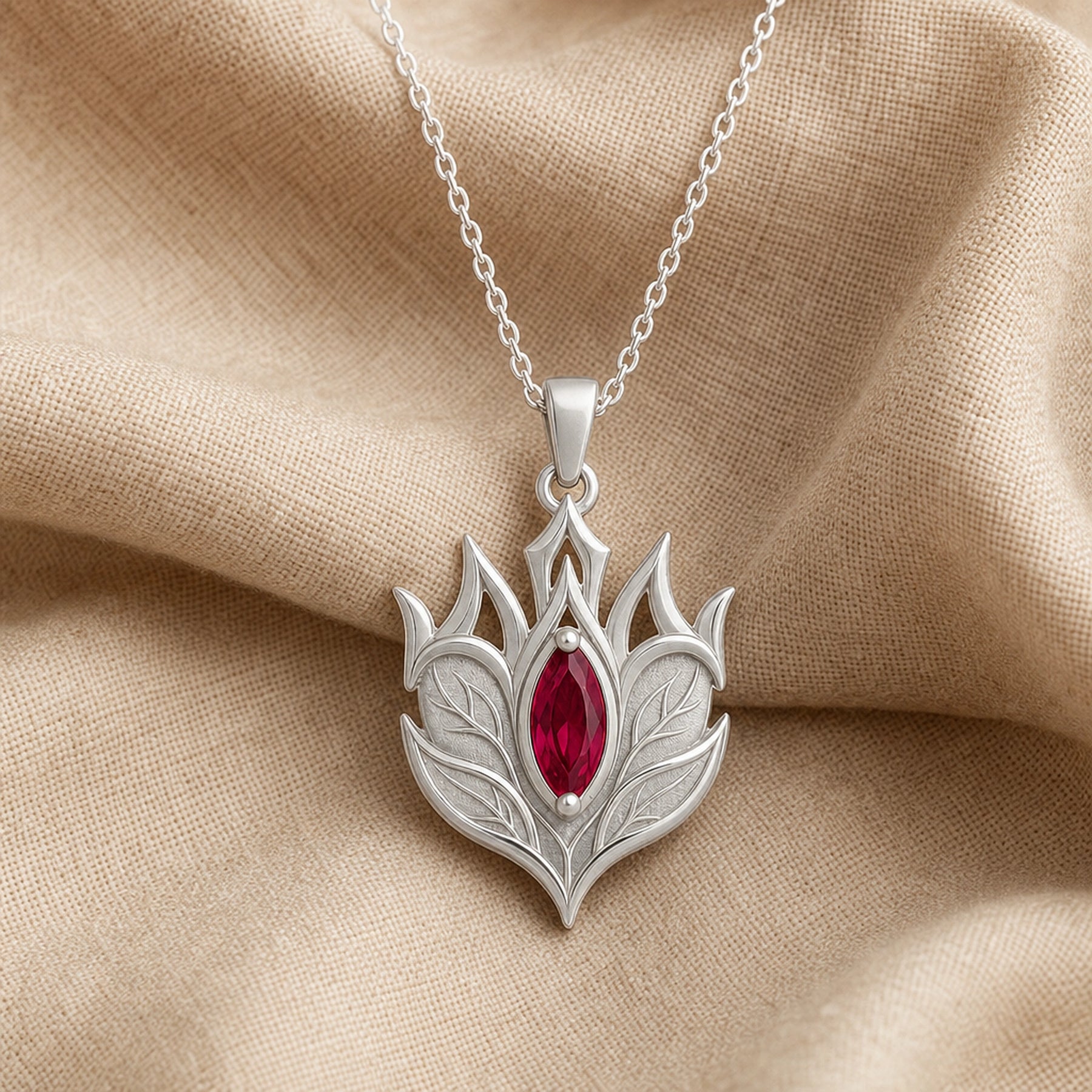 Ruby Elven Crownleaf pendant with layered engraved leaf details, pointed crown-like shapes, and a deep red marquise-shaped stone in a raised central setting. Silver finish.