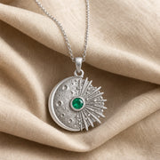 Kepler emerald supernova pendant with a cratered crescent moon, round green emerald center stone in a smooth setting, and detailed radiant starburst rays. Silver finish.