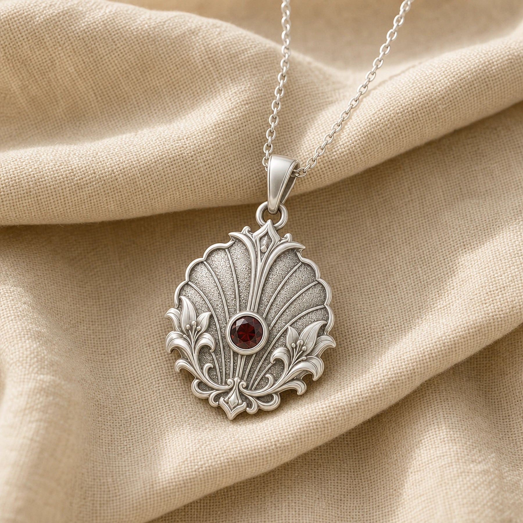 Imperial garnet lily shell pendant with a round deep-red stone in a smooth bezel, framed by raised lily flourishes and textured shell-like fan relief. Silver finish.