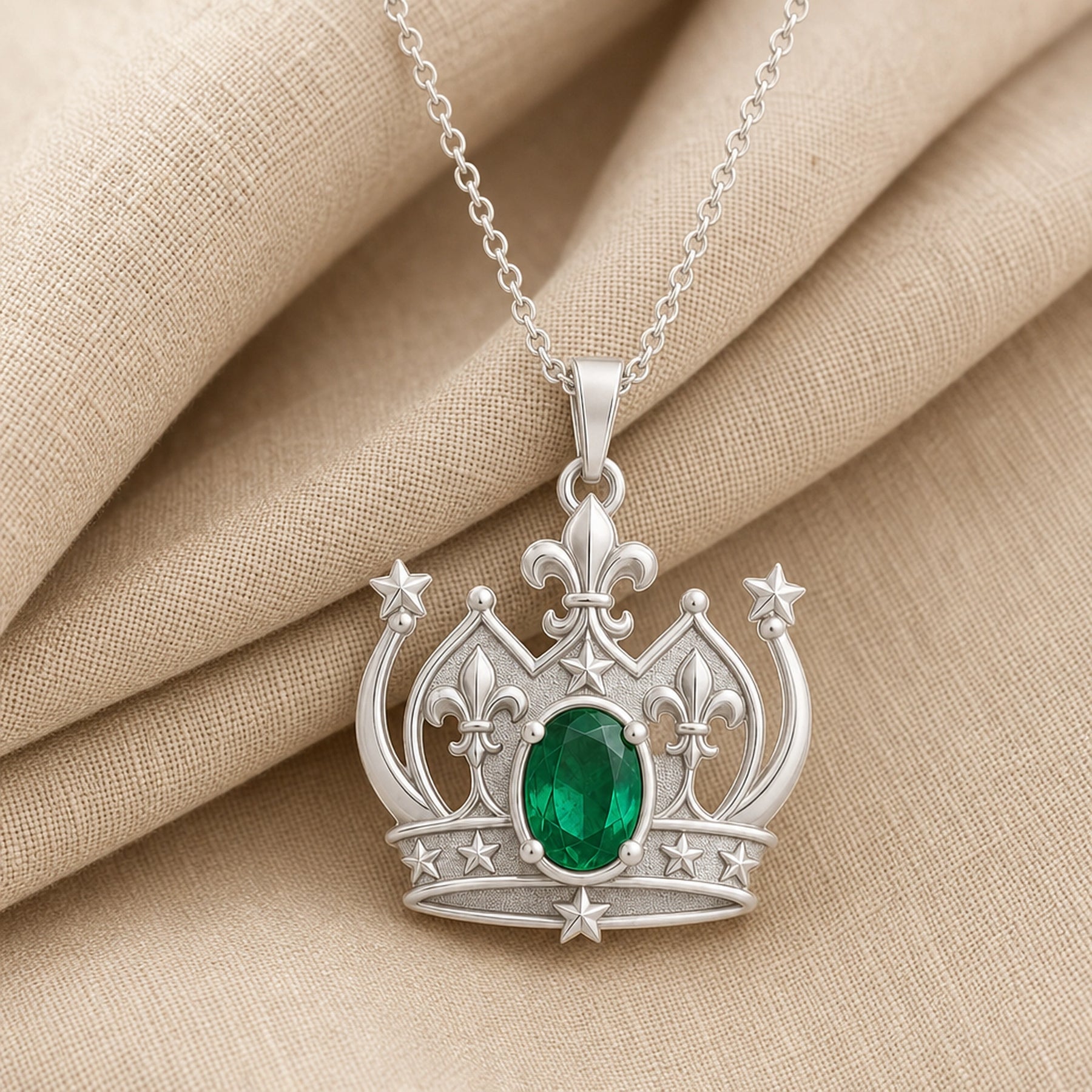 Emerald fleur-de-lis crown pendant with an oval green center stone in a raised prong setting, detailed star accents, sculpted crown arches, and ornate openwork metalwork. Silver finish.