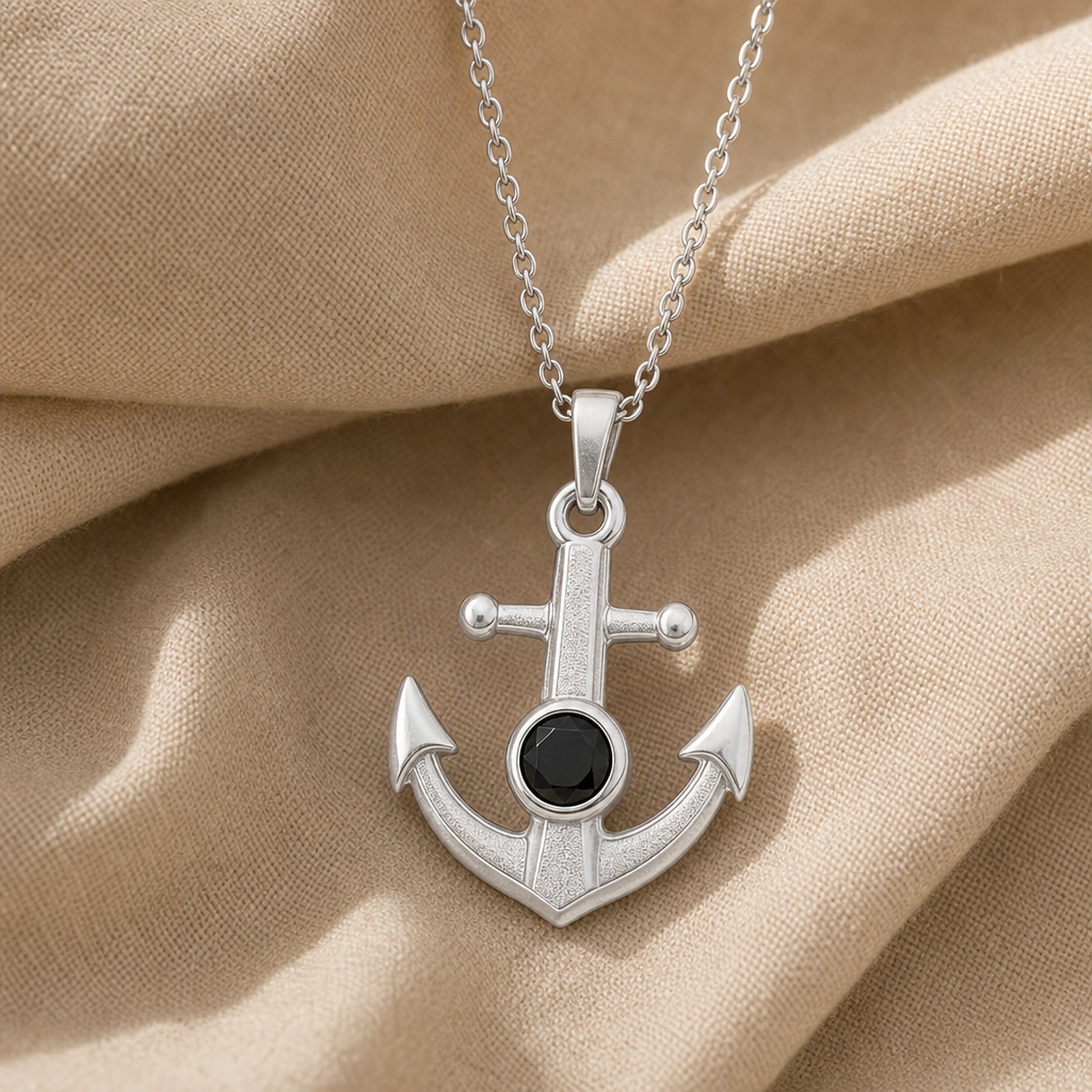 Black onyx anchor pendant with a faceted dark stone in a round bezel setting, raised textured center, polished arrowhead flukes, and cable chain. Silver finish.