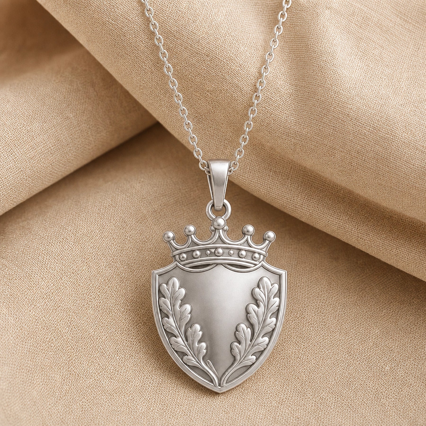 Oakleaf crown shield pendant with a pointed shield shape, raised botanical leaf relief, detailed crown top, smooth center panel, and a polished cable chain. Silver finish.
