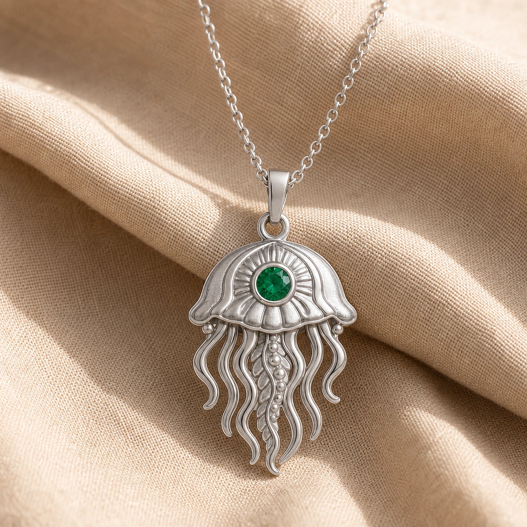 Emerald jellyfish pendant necklace with a round faceted green stone in a bezel-style setting, a textured domed bell, and flowing sculpted tentacles. Silver finish.