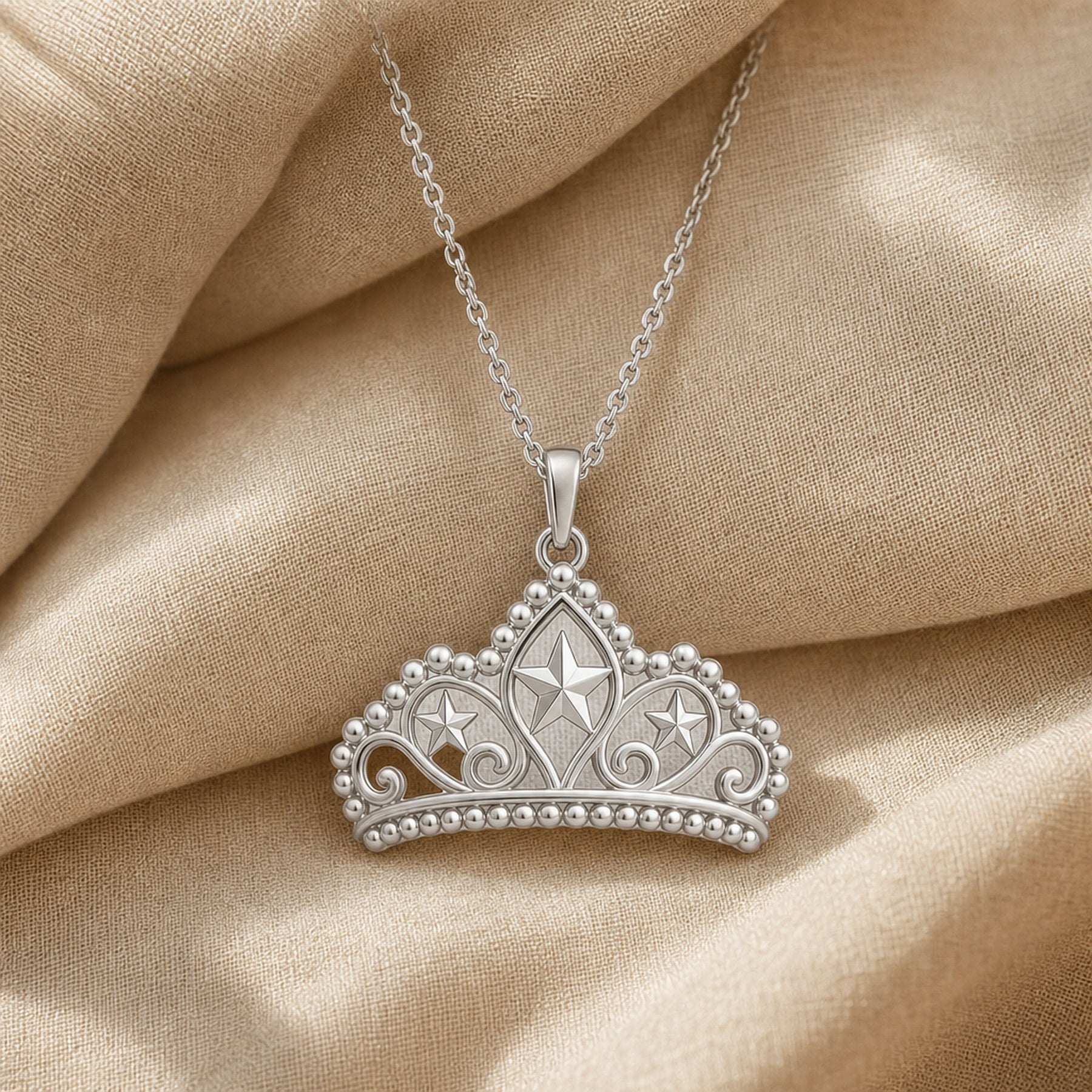 Pearl-bordered star tiara pendant with three raised star motifs, ornate openwork scrollwork, rounded bead edging, and a polished warm yellow-tone finish on a cable chain. Silver finish.