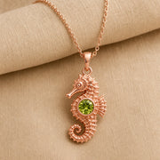 925 sterling silver seahorse pendant with a curled tail, sculpted marine details and a round green peridot centerpiece. Rose gold finish.