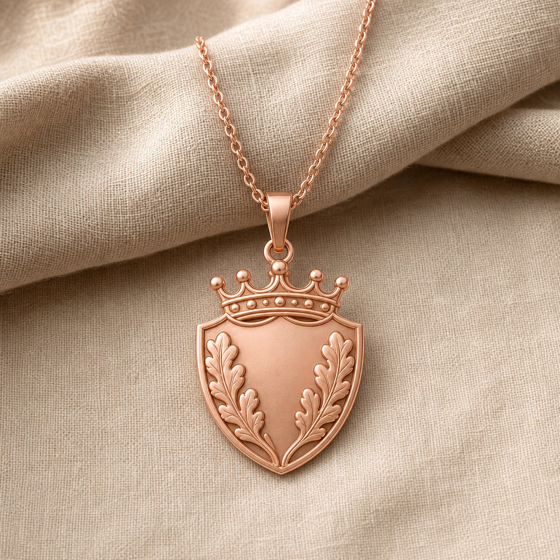 Oakleaf crown shield pendant with a pointed shield shape, raised botanical leaf relief, detailed crown top, smooth center panel, and a polished cable chain. Rose gold finish.