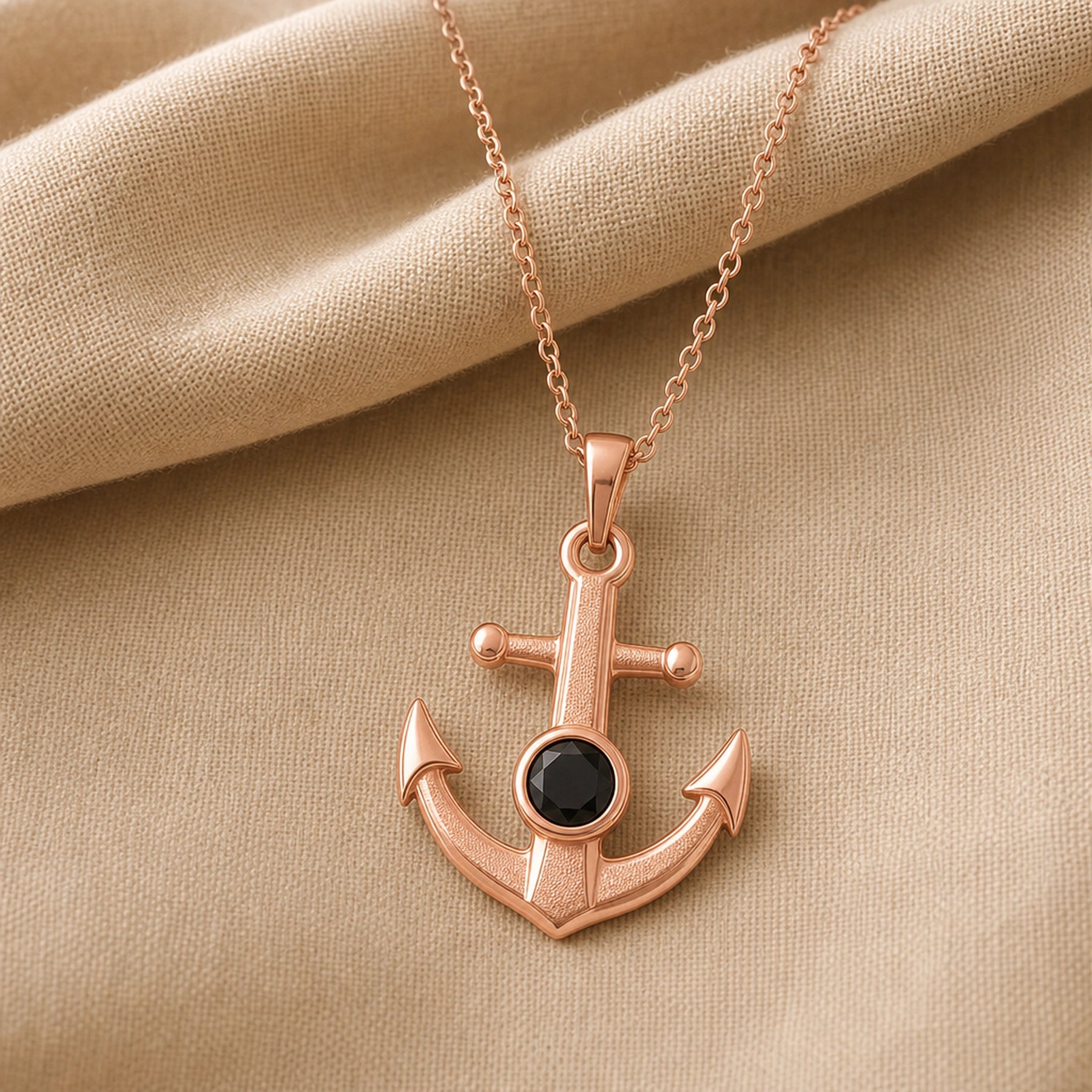 Black onyx anchor pendant with a faceted dark stone in a round bezel setting, raised textured center, polished arrowhead flukes, and cable chain. Rose gold finish.