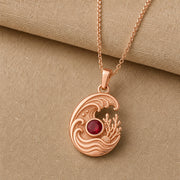 925 sterling silver tide pendant with curling ocean waves, coral and shell details, and a round ruby centerpiece. Rose gold finish.