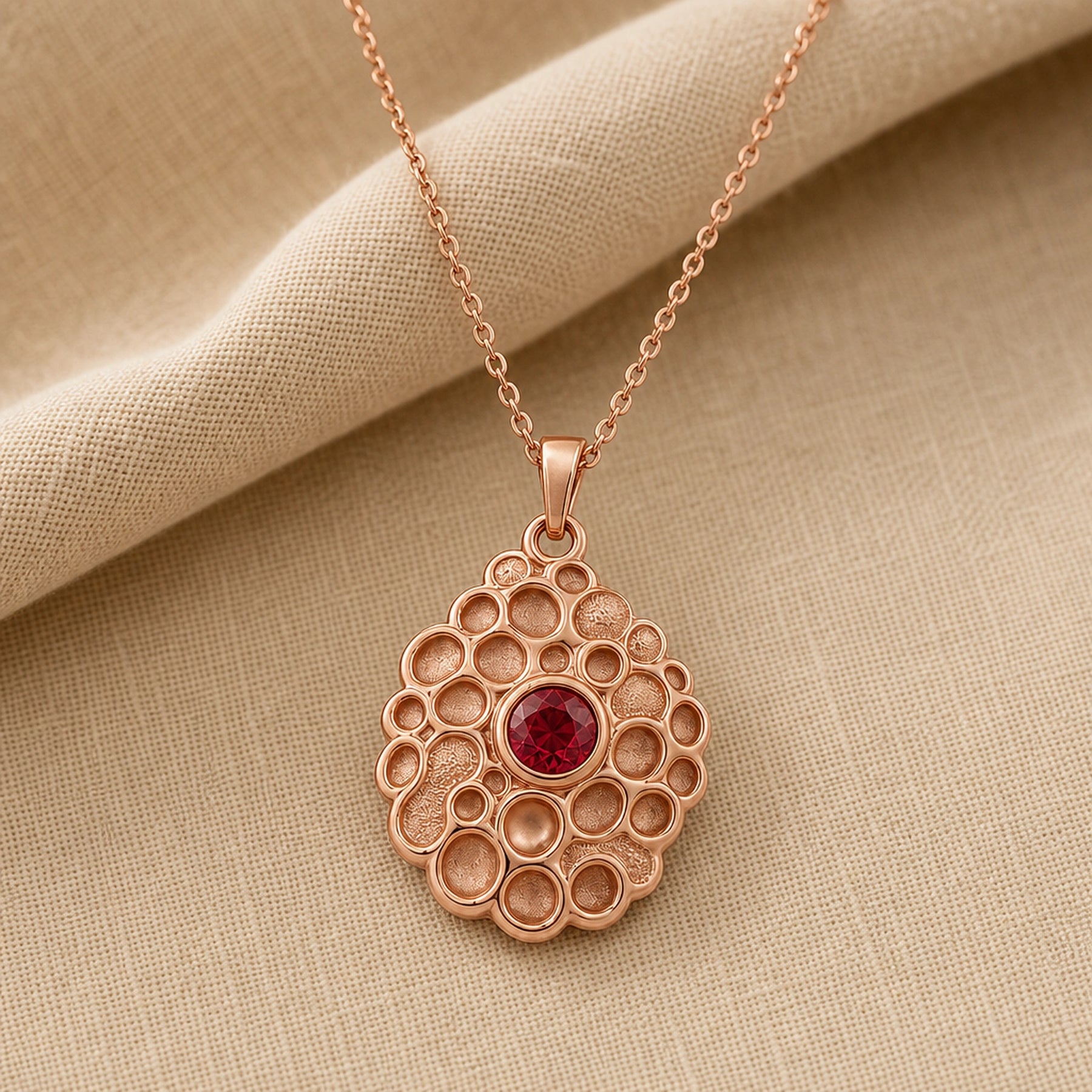 Ruby seafoam pendant with a round deep-red stone in a smooth bezel setting, surrounded by raised textured circular cells in an organic seafoam design on a cable chain. Rose gold finish.