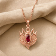 Ruby Elven Crownleaf pendant with layered engraved leaf details, pointed crown-like shapes, and a deep red marquise-shaped stone in a raised central setting. Rose gold finish.