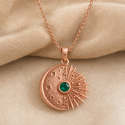 Kepler emerald supernova pendant with a cratered crescent moon, round green emerald center stone in a smooth setting, and detailed radiant starburst rays. Rose gold finish.