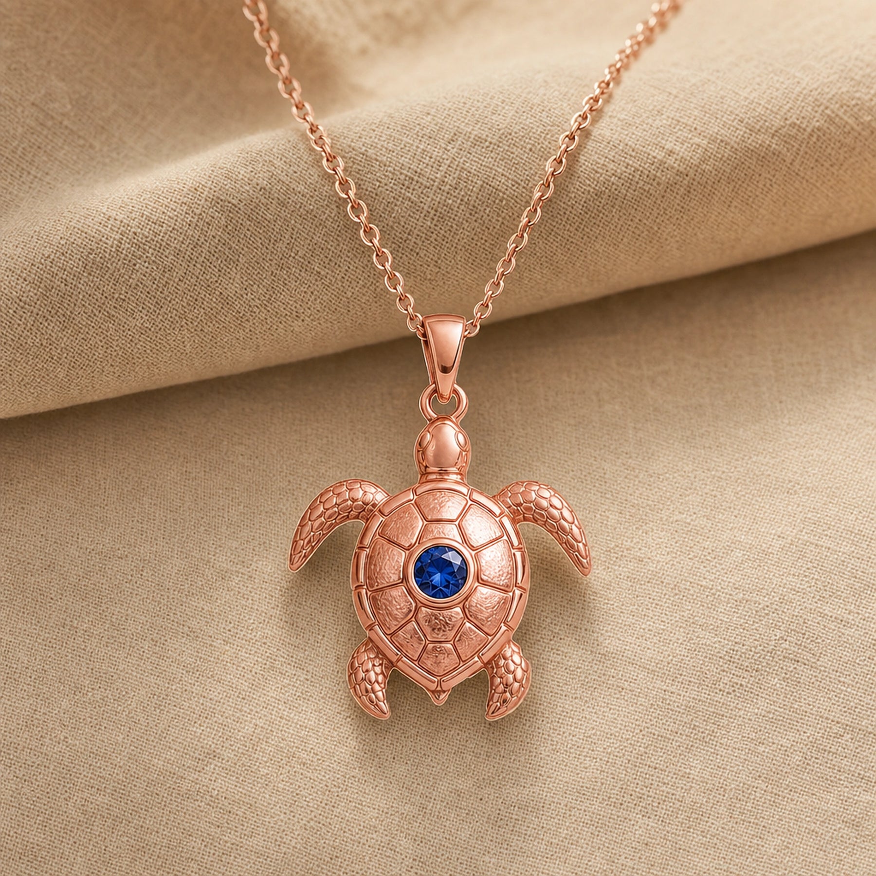 925 sterling silver sea turtle pendant with patterned shell plates, textured flippers and a round blue sapphire centerpiece. Rose gold finish.
