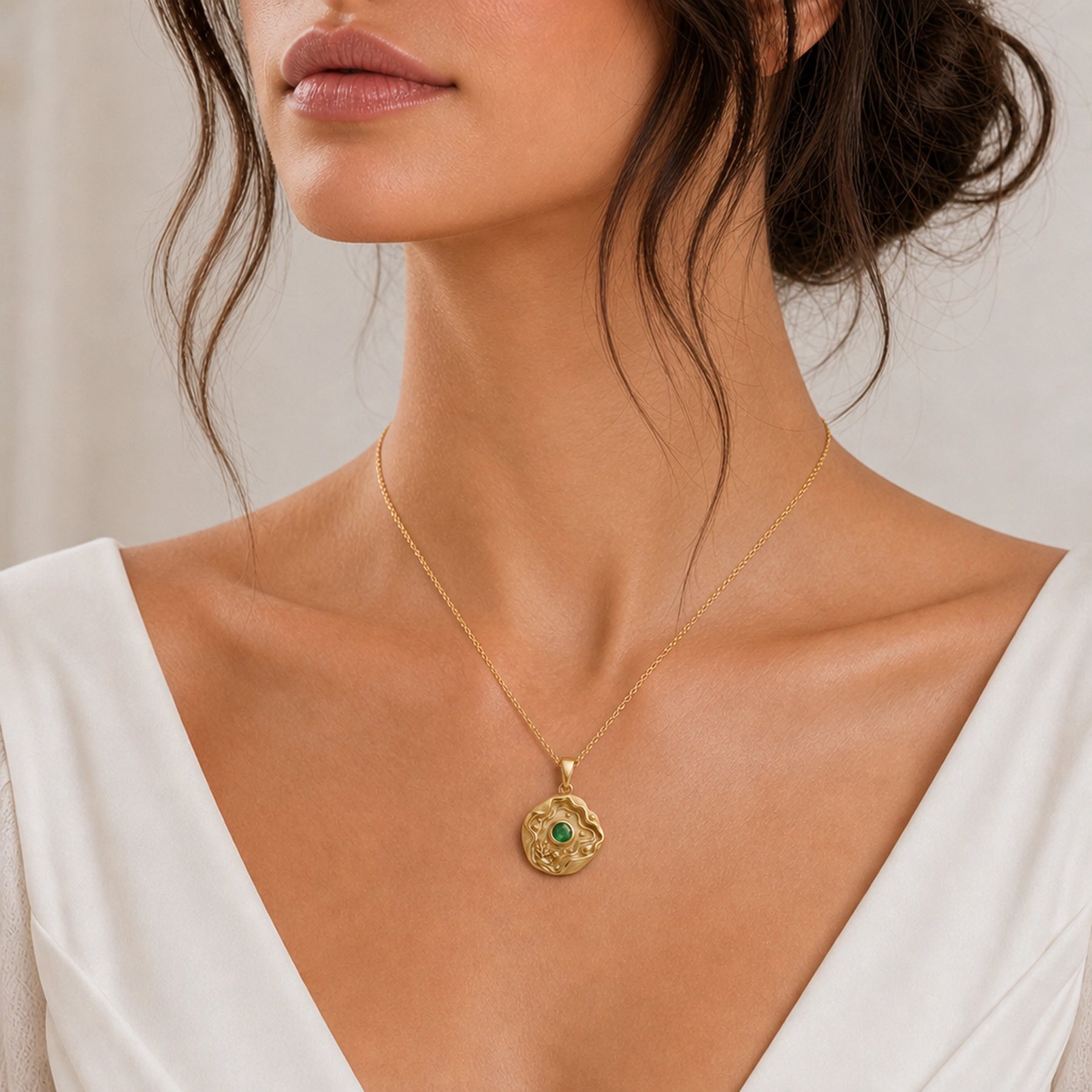 Emerald tide pool pendant necklace with a faceted green center stone in a bezel setting, surrounded by layered wave relief, shell details, coral-inspired accents, and textured ocean motifs. Worn on a model, front view.