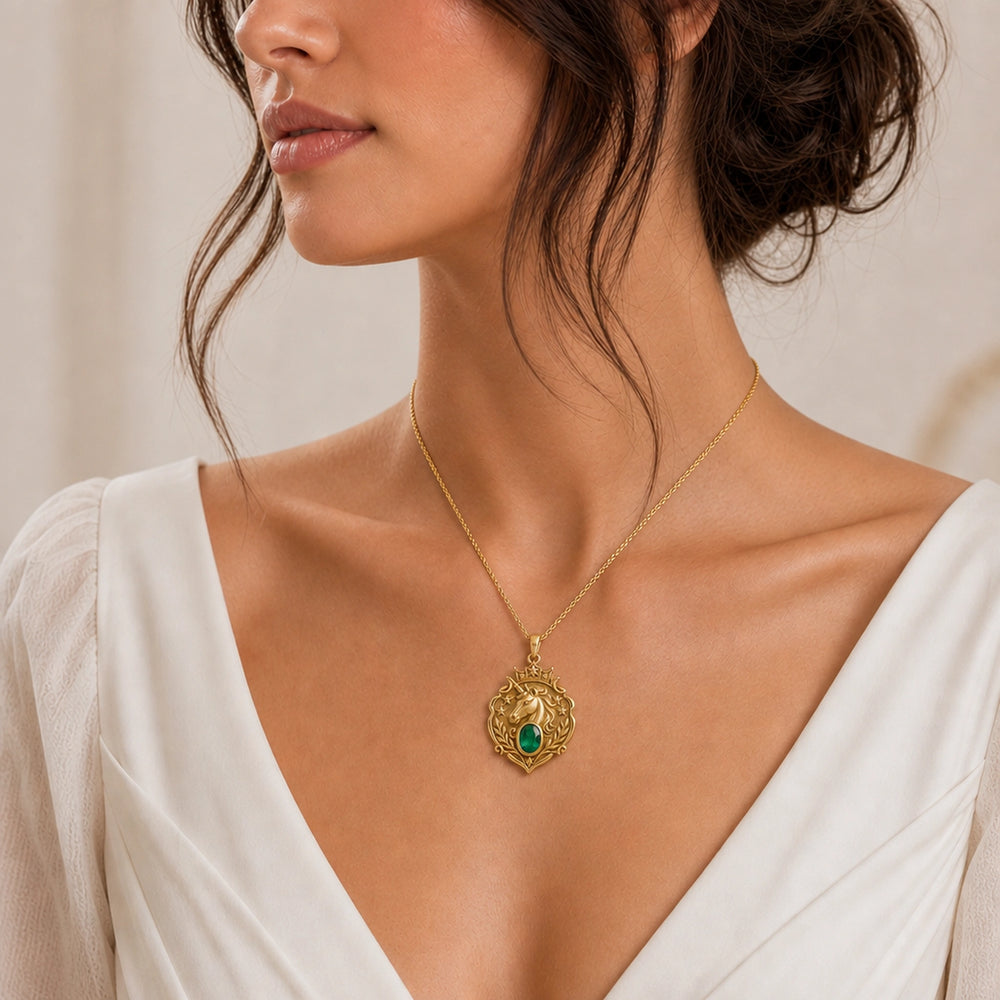 Emerald Unicorn Starcrest Pendant with a sculpted unicorn head, raised stars and leaf details, and an oval faceted green emerald in a framed center setting. Worn on a model, front view.