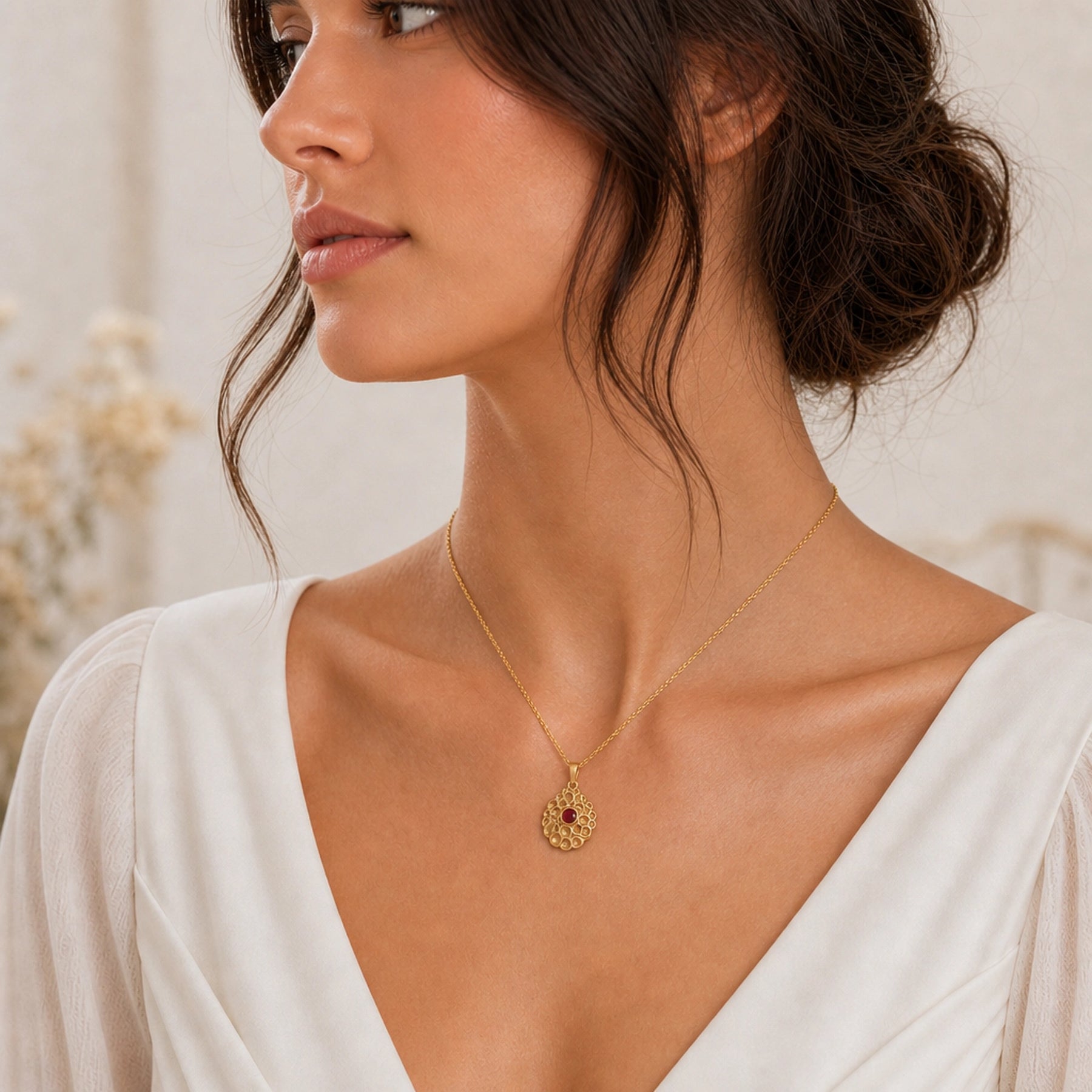 Ruby seafoam pendant with a round deep-red stone in a smooth bezel setting, surrounded by raised textured circular cells in an organic seafoam design on a cable chain. Worn on a model, angled view.