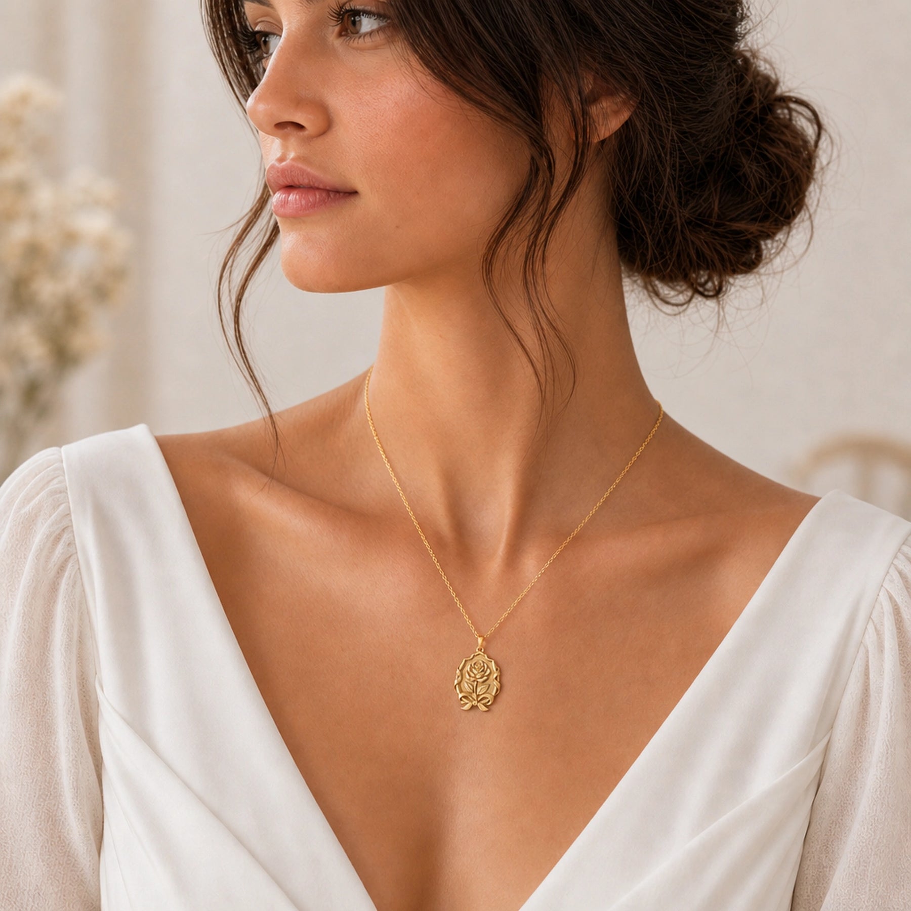 Duchess rose ribbon emblem pendant with a raised floral relief, engraved leaves, flowing ribbon frame, bow detail, and polished warm-toned finish. Worn on a model, angled view.