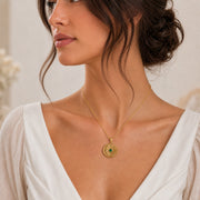 Kepler emerald supernova pendant with a cratered crescent moon, round green emerald center stone in a smooth setting, and detailed radiant starburst rays. Worn on a model, angled view.