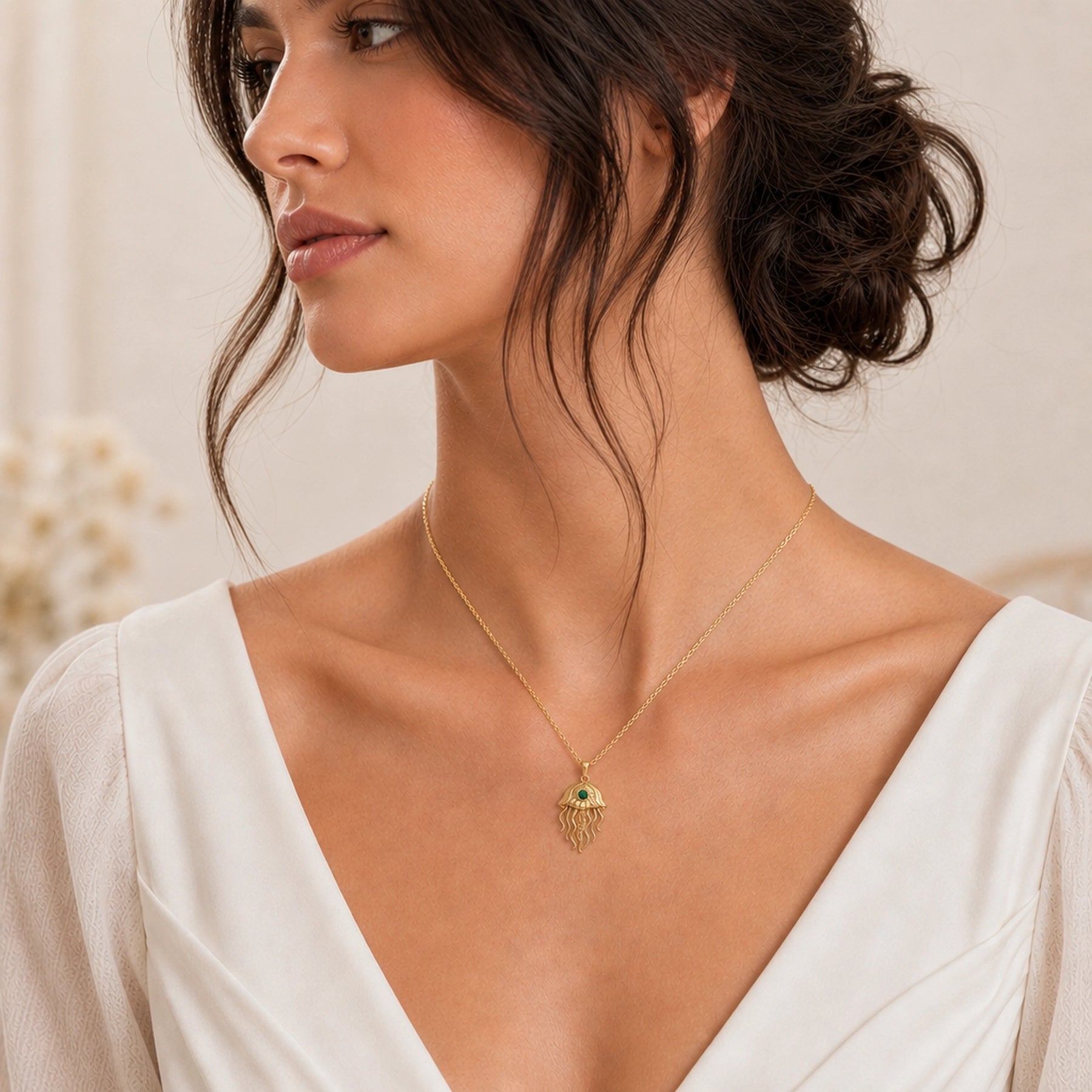 Emerald jellyfish pendant necklace with a round faceted green stone in a bezel-style setting, a textured domed bell, and flowing sculpted tentacles. Worn on a model, angled view.